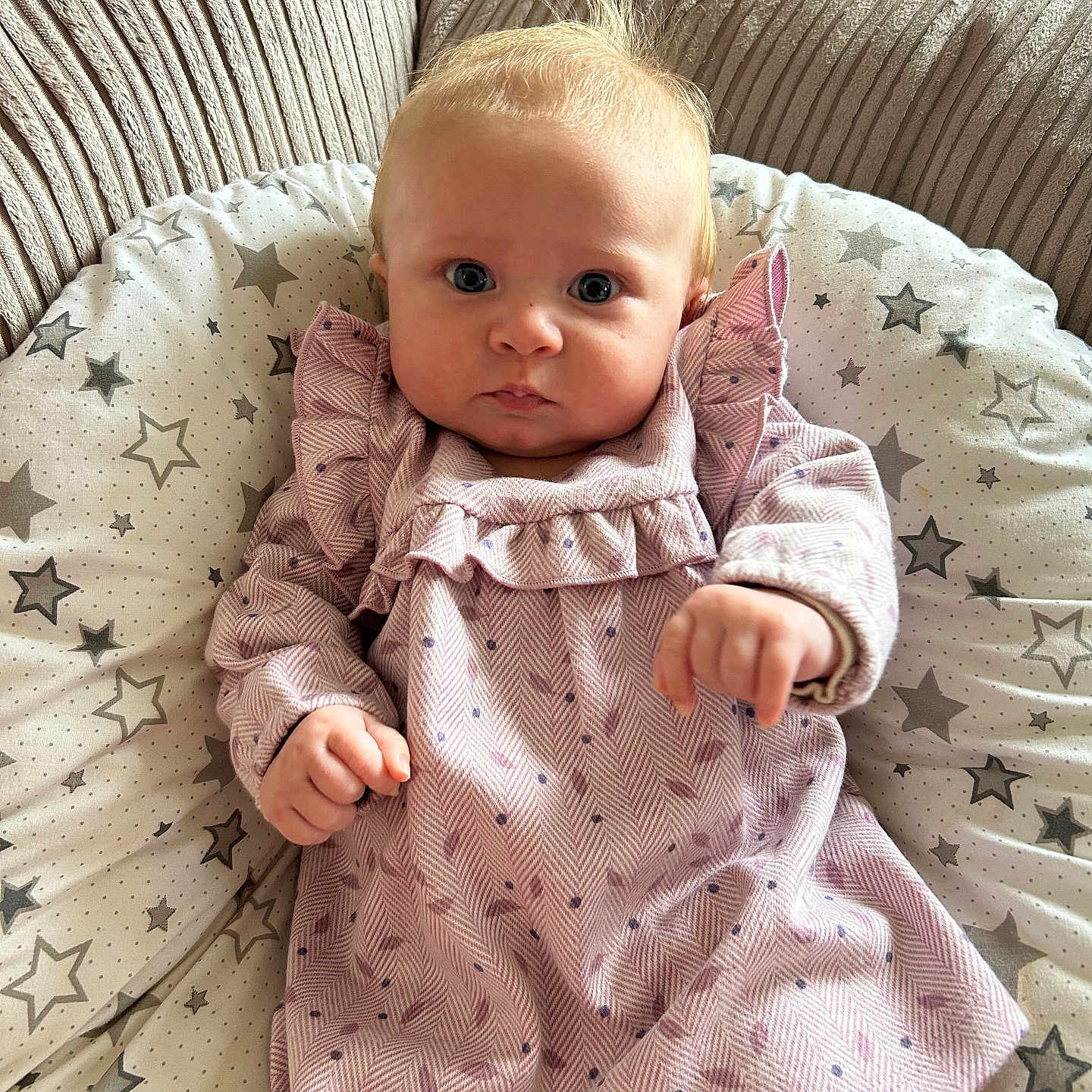 Maeve joined the competition — help win amazing prizes! baby, beige, child, comfort, curious, cushion, cute, face, hands, home, indoor, infant, patterned_clothing, pink_dress, portrait, seated, sofa, star_pattern, toddler, young_child