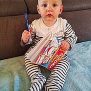 Théo a rejoint le concours — aidez-le/la à gagner de superbes lots ! baby, blue_blanket, child, couch, curious, expression, face, feet, hands, home, indoor, pen, person, playful, puzzle_book, reading, seated, soft_texture, striped_pajamas, young_child