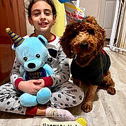 Oliver is registered to the contest to win money with this photo: child, dog, birthday_hat, plush_toy, pajamas, birthday_treat, bone_shaped_cookie, indoor, floor, smiling, celebration, pet, toy, happy, cute, sitting, party, home, clothing, fur