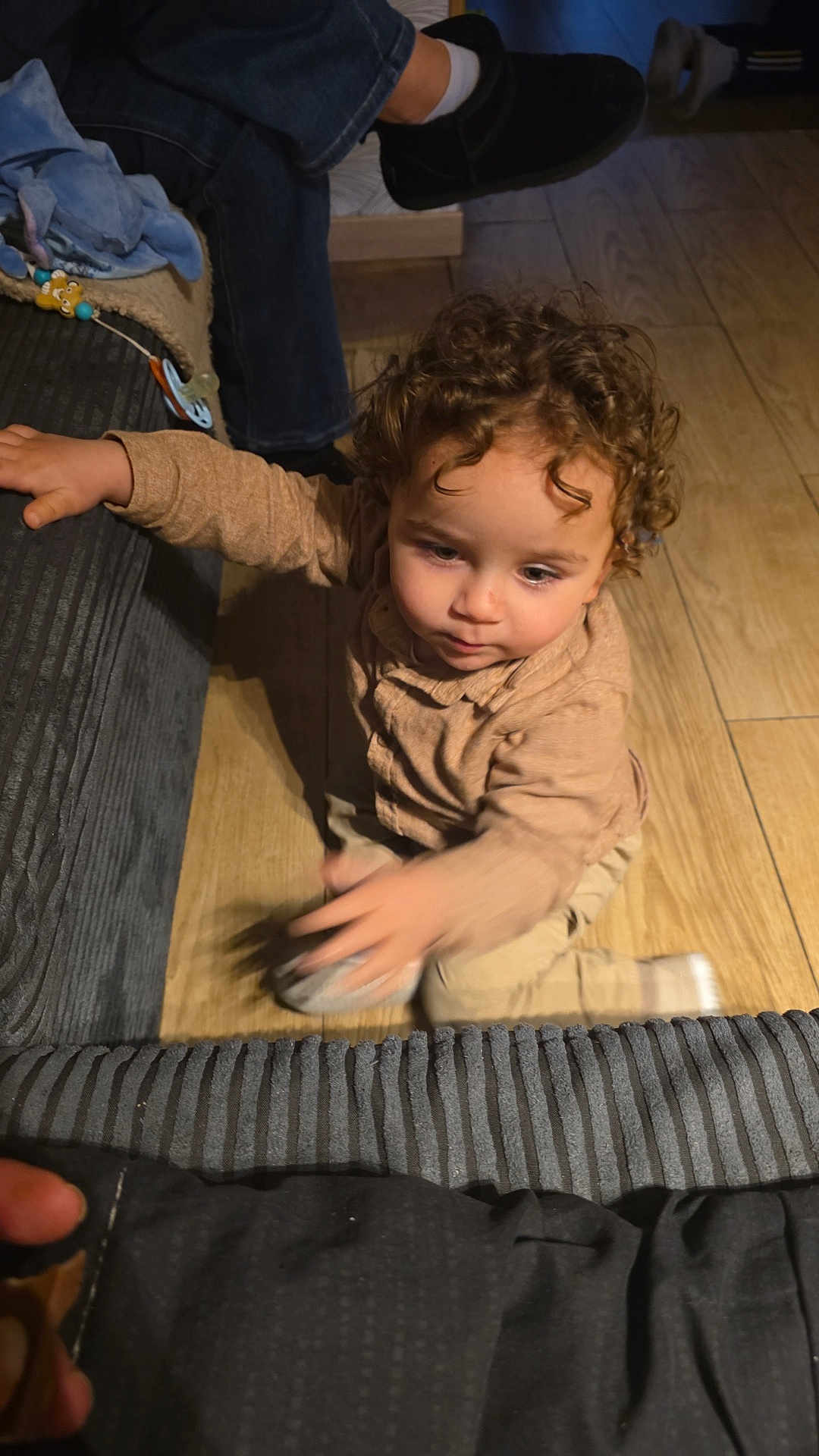 Yassine a rejoint le concours — aidez-le/la à gagner de superbes lots ! child, toddler, curly_hair, reaching, motion_blur, indoor, wooden_floor, couch, sofa, clothing, hand, face, sitting, toy, pacifier, adult_leg, slipper, sock, floor, home
