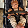 Izak participe au concours pour gagner de l'argent avec cette photo : baby, child, stroller, smiling, cap, brown_clothing, striped_pants, barefoot, indoor, flooring, flower_vase, chair, happy_expression, seatbelt, black_stroller, wooden_floor, hand, foot, person, portrait
