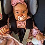 baby, child, pacifier, headband, pink_clothing, car_seat, safety_harness, plush_toy, blanket, infant, cute, portrait, indoor, face, hands, button, fabric, soft_toy, smile, young