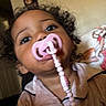 accessory, baby, casual, child, close_up, clothing, curly_hair, cute, expression, face, home, indoor, pacifier, person, pink, portrait, soft_lighting, toddler, wall_art, young_child