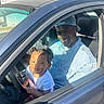 Nova is registered to the contest to win money with this photo: adult, cap, car, casual, child, denim_jacket, family, happy, inside, joy, person, portrait, seat, shadow, smile, steering_wheel, sunlight, toddler, vehicle, window