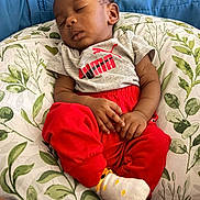 Keziah is registered to the contest to win money with this photo: baby, child, clothing, comfort, couch, cushion, grey_shirt, home, indoor, infant, leaf_pattern, nap, peaceful, person, pillow, red_pants, relaxation, skin, sleeping, socks