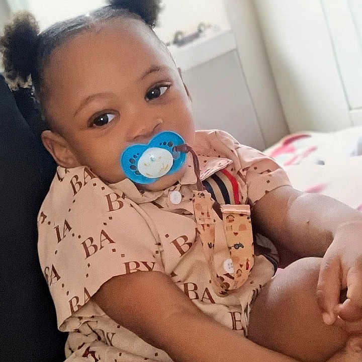 Danny joined the competition — help win amazing prizes! baby, child, infant, portrait, sitting, pacifier, hair_puffs, smiling, indoors, bedroom, bed, clothing, patterned_outfit, blue_pacifier, person, face, eyes, arms, family, home
