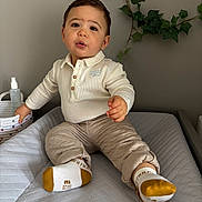 Enea a rejoint le concours — aidez-le/la à gagner de superbes lots ! baby, changing_pad, child, clothing, curious, expression, face, footwear, greenery, hands, home, indoor, ivy, pants, portrait, shirt, sitting, socks, toddler, wall