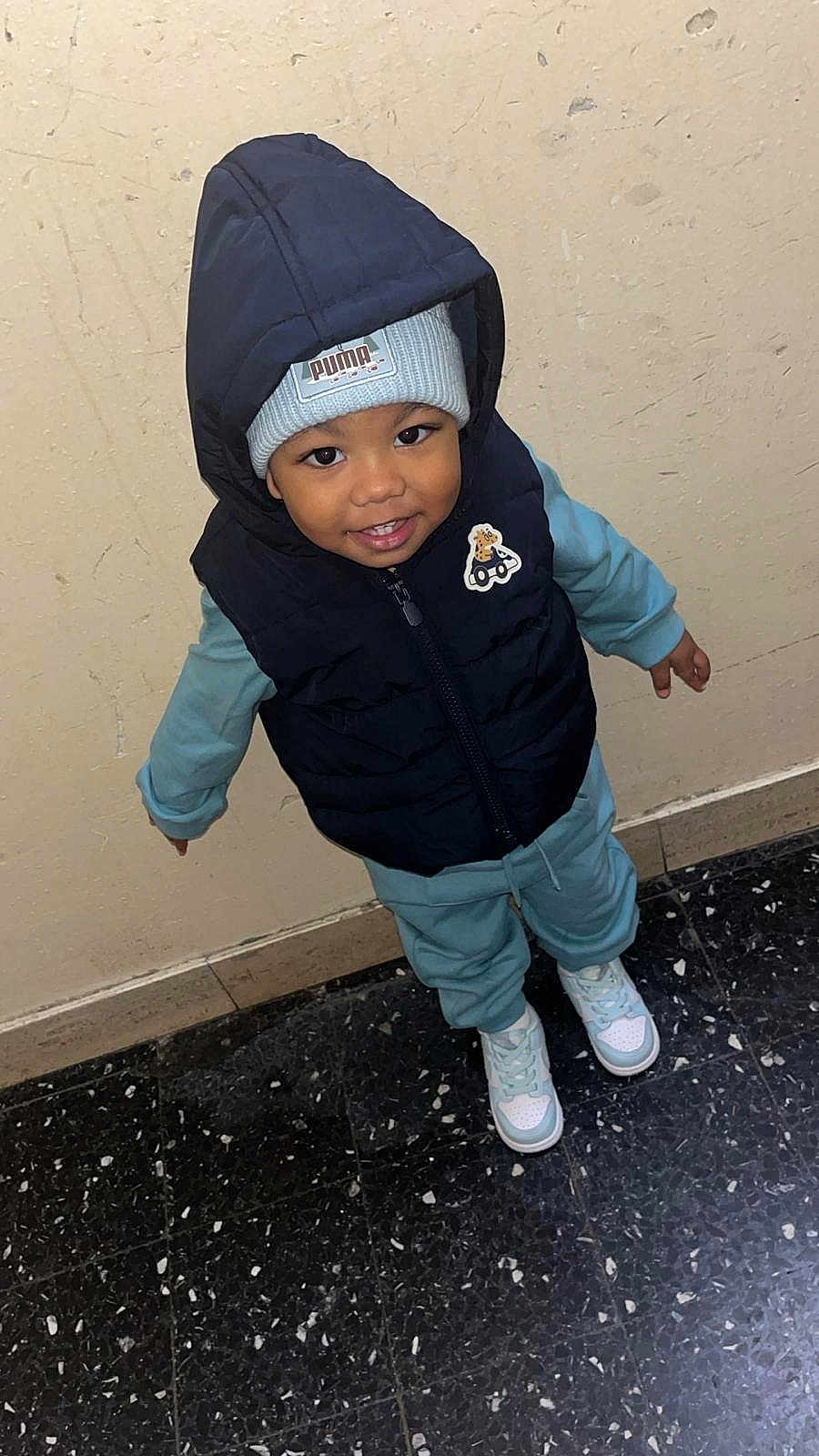 Jayden Daniel participe au concours pour gagner de l'argent avec cette photo : child, toddler, smiling, hooded_vest, beanie, puma, blue_clothing, sneakers, indoor, floor, wall, standing, cute, portrait, fashion, winter, happy, person, young_child, casual_wear