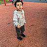 Josh joined the competition — help win amazing prizes! child, boy, playground, park, swing, swingset, outdoor, portrait, standing, hoodie, sweatpants, sneakers, gray_clothing, playground_surface, red_poles, blue_equipment, grass, trees, background_people, daylight