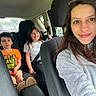 child, children, mother, family, car, car_interior, selfie, portrait, smiling, seated, seatbelt, backseat, road_trip, vehicle, boy, girl, adult, indoors, casual_clothing, photograph