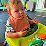 baby, child, toddler, sitting, activity_walker, bib, snack, food, smiling, face, portrait, outdoor, patio, colorful, toy, infant, clothing, chair, home, daylight