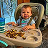 toddler, child, baby, smiling, high_chair, eating, food, vegetables, corn, meal, tray, indoor, portrait, happy, sitting, bib, safety_harness, cup, kitchen, home