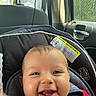 baby, infant, child, smiling, happy, portrait, face, eyes, teeth, car_seat, vehicle, seatbelt, harness, indoors, automobile, close_up, red_clothing, safety, daylight, photograph