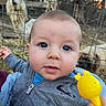 baby, child, infant, portrait, face, blue_eyes, wide_eyed, outdoor, farm, goat, animal, fence, hay, barn, toy, yellow_toy, blue_clothing, gray_jacket, hand, close_up