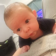 Quincy is registered to the contest to win money with this photo: baby, infant, face, head, eyes, skin, hand, tummy_time, clothing, black_shirt, expression, curious, indoors, blurred_background, person, child, young, cute, portrait, laying_down