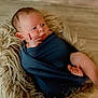 Quincy is registered to the contest to win money with this photo: baby, infant, wrapped, blue_cloth, fluffy_rug, curious, face, hand, foot, skin, newborn, lying_down, soft_texture, indoors, cute, portrait, child, expression, cozy, peaceful