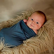 Quincy joined the competition — help win amazing prizes! baby, infant, wrapped, blue_cloth, fur_basket, soft_texture, curious_look, face, skin, newborn, portrait, cute, cozy, lying_down, indoors, warm_lighting, head, hand, peaceful, child