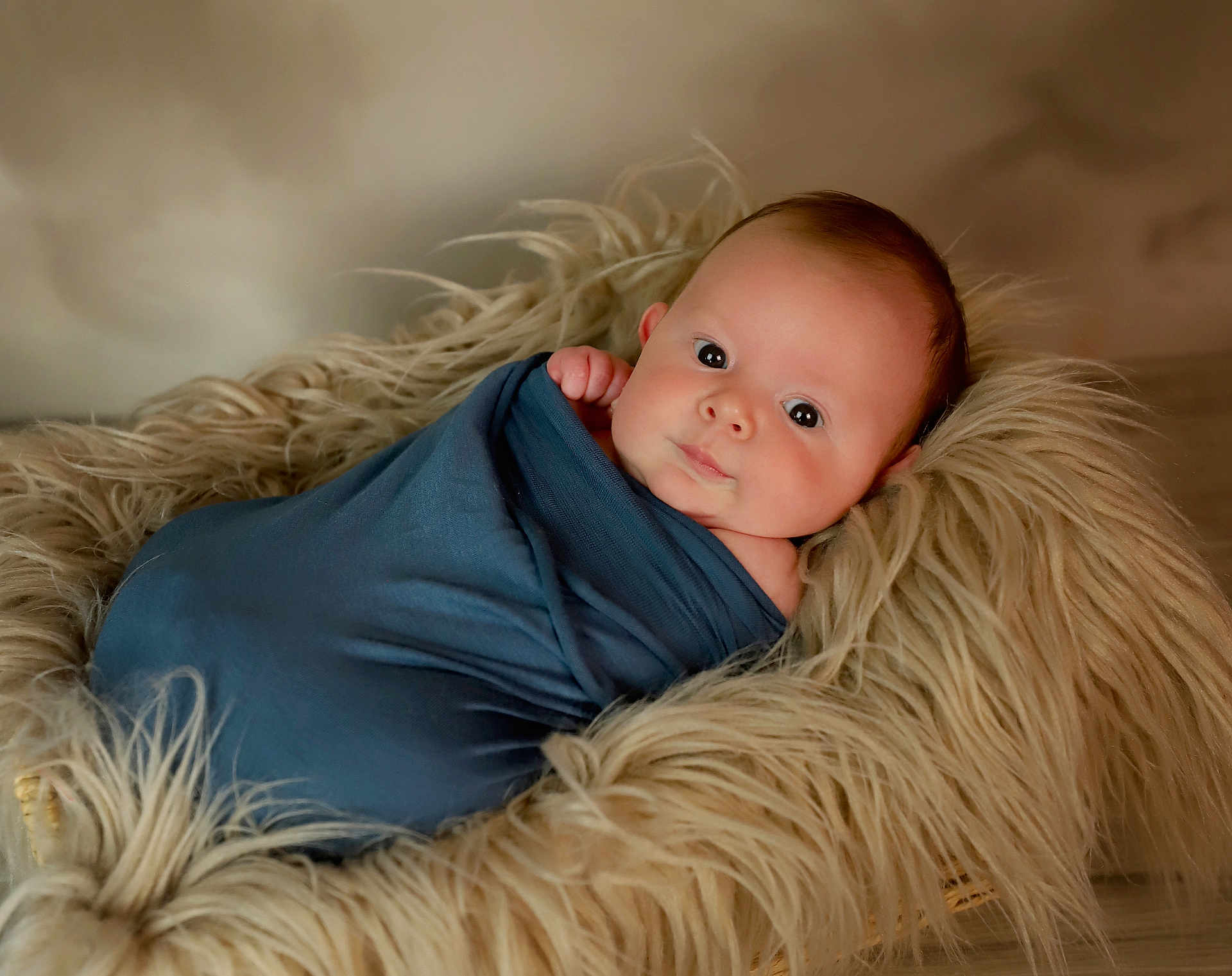 Quincy joined the competition — help win amazing prizes! baby, infant, wrapped, blue_cloth, fur_basket, soft_texture, curious_look, face, skin, newborn, portrait, cute, cozy, lying_down, indoors, warm_lighting, head, hand, peaceful, child