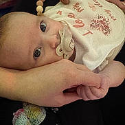 Evelyn joined the competition — help win amazing prizes! baby, baby_accessory, beaded_necklace, bib, close_up, clothing, curious_eyes, cute, face, hand, holding_hand, indoor, infant, pacifier, person, portrait, skin, tender_moment, warm_lighting, young_child