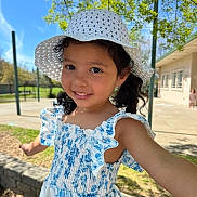 Hailey joined the competition — help win amazing prizes! blue_flower_pattern, building, casual_clothing, child, curly_hair, daylight, dress, earrings, girl, greenery, happy, hat, nature, outdoor, person, playground, portrait, smiling, sunhat, sunny