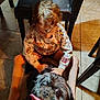 animal, black_dog, casual_clothing, chair, child, curly_hair, cute, dog, floor, foot, happy, human, indoor, petting, playful, sitting, smiling, tile_floor, toddler, tongue_out