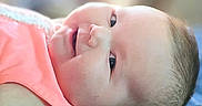 Mallory is registered to the contest to win money with this photo: baby, infant, smiling, face, portrait, close_up, lying_down, coral_clothing, skin, head, expression, happy, cute, child, young, indoors, soft_light, blurred_background, person, newborn