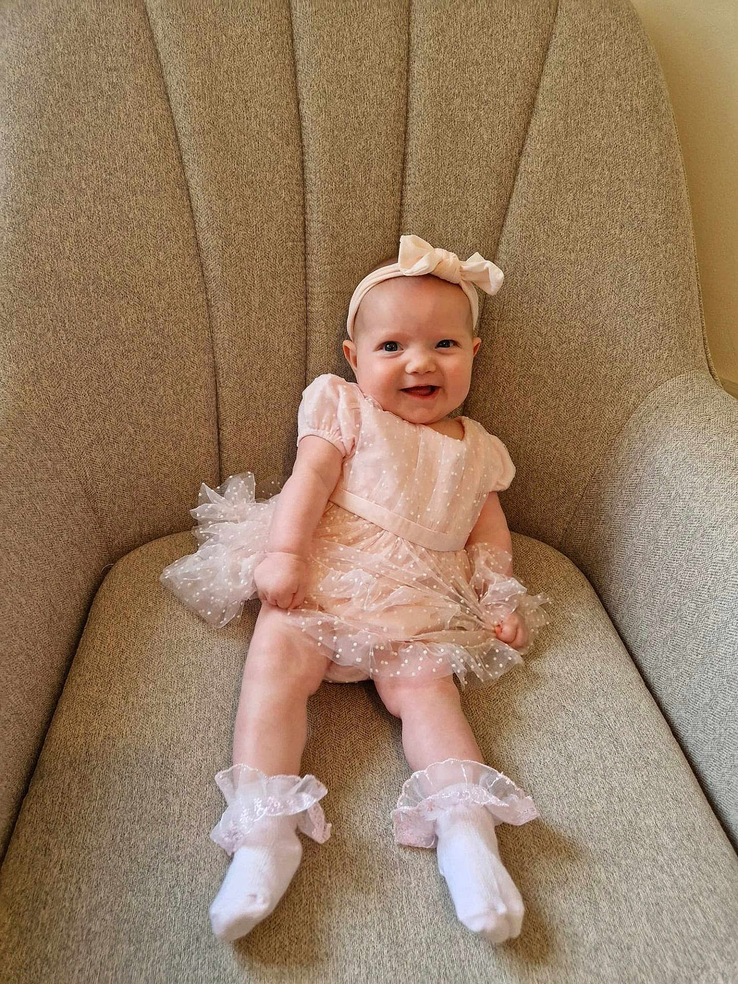 Evie is registered to the contest to win money with this photo: baby, child, smiling, dress, headband, socks, chair, indoor, cute, happy, infant, portrait, sitting, fabric, furniture, person, young, apparel, tulle, frills