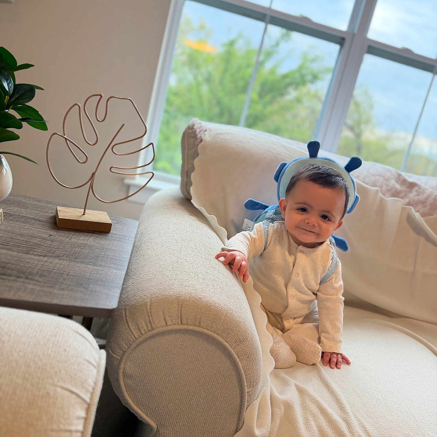 Ali is registered to the contest to win money with this photo: baby, child, infant, smile, pajamas, headband, blue, couch, blanket, living_room, window, plant, table, decor, furniture, indoors, cozy, cute, portrait, happy