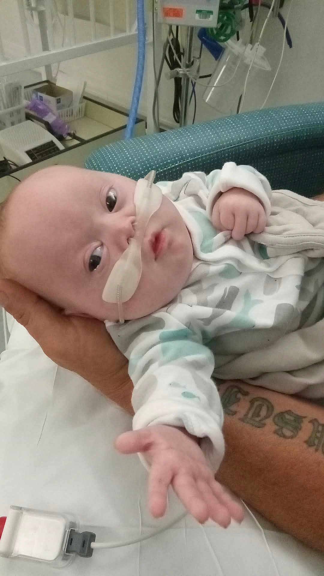 Scott joined the competition — help win amazing prizes! baby, infant, hospital, medical_equipment, oxygen_tube, hand, tattoo, bed, blanket, person, face, clothing, healthcare, patient, indoor, caregiver, monitoring_device, reaching_hand, hospital_room, comfort