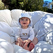 Louis a rejoint le concours — aidez-le/la à gagner de superbes lots ! baby, child, smiling, hat, onesie, cushion, outdoor, sunlight, blue_sky, green_foliage, happy, barefoot, portrait, infant, cute, sitting, face, nature, daylight, comfortable