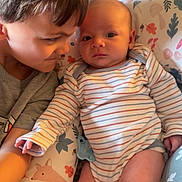 Leviticus is registered to the contest to win money with this photo: baby, child, siblings, striped_onesie, cushion, patterned_cushion, smile, curious, indoor, cozy, infant, cute, family, toddler, bedroom, soft_lighting, portrait, love, togetherness, relaxed