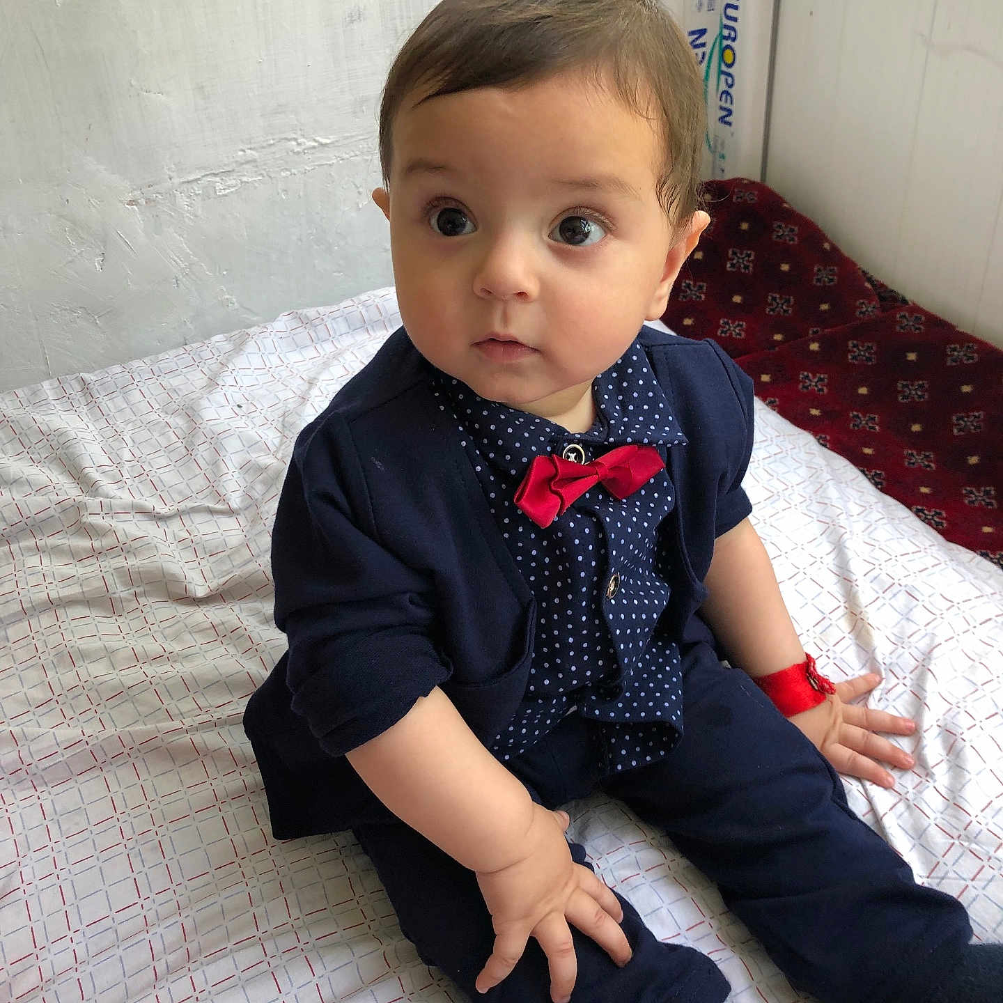 Sohrab is registered to the contest to win money with this photo: baby, bedspread, bow_tie, child, clothing, curious, cute, face, fashion, indoor, infant, navy_blue, person, polka_dot, portrait, red, sitting, socks, wristband, young_child