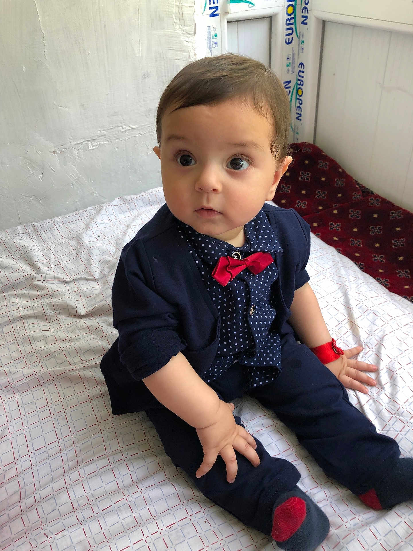 Sohrab is registered to the contest to win money with this photo: baby, child, infant, sitting, clothing, bow_tie, polka_dot, navy_blue, red, socks, wristband, bedspread, indoor, curious, face, cute, portrait, person, young_child, fashion