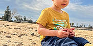 Sohrab joined the competition — help win amazing prizes! boots, boy, casual_clothing, child, cloudy_sky, curious, daylight, hands, landscape, nature, navy_pants, outdoor, portrait, relaxed, rocks, sand, short_hair, sitting, trees, yellow_shirt