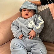 Zaviyar is registered to the contest to win money with this photo: baby, infant, child, blue_clothing, bucket_hat, couch, pillow, hand, indoor, casual, cute, portrait, sitting, furniture, expression, skin, foot, sleeve, relaxed, cozy