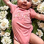 baby, pink_onesie, smiling, flower, white_flower, green_blanket, infant, cute, lying_down, happy, child, face, skin, arms, legs, nature, soft_texture, portrait, closeup, adorable
