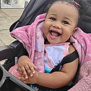 Amarie is registered to the contest to win money with this photo: baby, child, smiling, stroller, pink_blanket, blanket, sippy_cup, hand, teeth, laughing, portrait, outdoor, pavement, seatbelt, bow, dark_hair, rosy_cheeks, clothing, cute, joyful