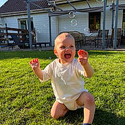 Télyo a rejoint le concours — aidez-le/la à gagner de superbes lots ! toddler, child, grass, bubbles, outdoor, smiling, sunlight, house, patio, white_shirt, sock, playtime, happy, daytime, greenery, baby, lawn, kneeling, joy, summer