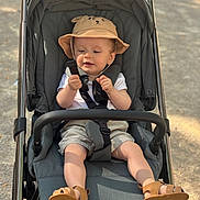 Timothée participe au concours pour gagner de l'argent avec cette photo : toddler, child, stroller, hat, outdoor, sunlight, shoes, shorts, white_shirt, baby, baby_toddler, sitting, curious, straps, footwear, summer, playful, cute, infant, recreation