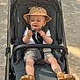 toddler, child, stroller, hat, outdoor, sunlight, shoes, shorts, white_shirt, baby, baby_toddler, sitting, curious, straps, footwear, summer, playful, cute, infant, recreation