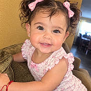 Celina is registered to the contest to win money with this photo: child, toddler, girl, smiling, portrait, indoors, couch, sitting, pink_bows, floral_dress, curly_hair, brown_hair, eyes, happy, baby, home, furniture, close_up, photograph, phone_screenshot