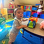 Christopher is registered to the contest to win money with this photo: toddler, child, toy, train, playroom, colorful, carpet, table, chair, shelf, plastic_toy, indoor, person, shorts, socks, expression, curious, play, kids, furniture