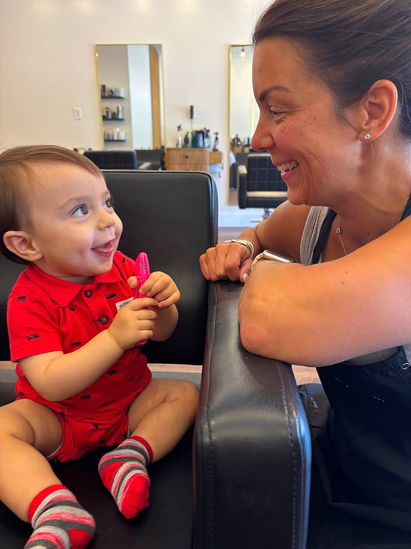 Christopher is registered to the contest to win money with this photo: armrest, baby, black_chair, chair, child, face, happy, indoor, interaction, marker, mirror, person, playing, red_clothing, reflection, shorts, skin, smiling, socks, woman