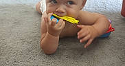 Luke is registered to the contest to win money with this photo: baby, blue, carpet, chewing, child, crawling, curious, diaper, floor, goggles, hand, indoor, infant, orange, person, plastic, playful, red_chair, toy, yellow