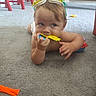 baby, child, carpet, goggles, toy, indoor, floor, plastic, chewing, hand, red_chair, yellow, blue, orange, person, playful, curious, crawling, infant, diaper