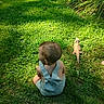 child, toddler, grass, outdoor, lizard, bearded_dragon, greenery, plants, sunlight, shade, summer, nature, backyard, reptile, curious, overalls, baby, animal, pet, exploration