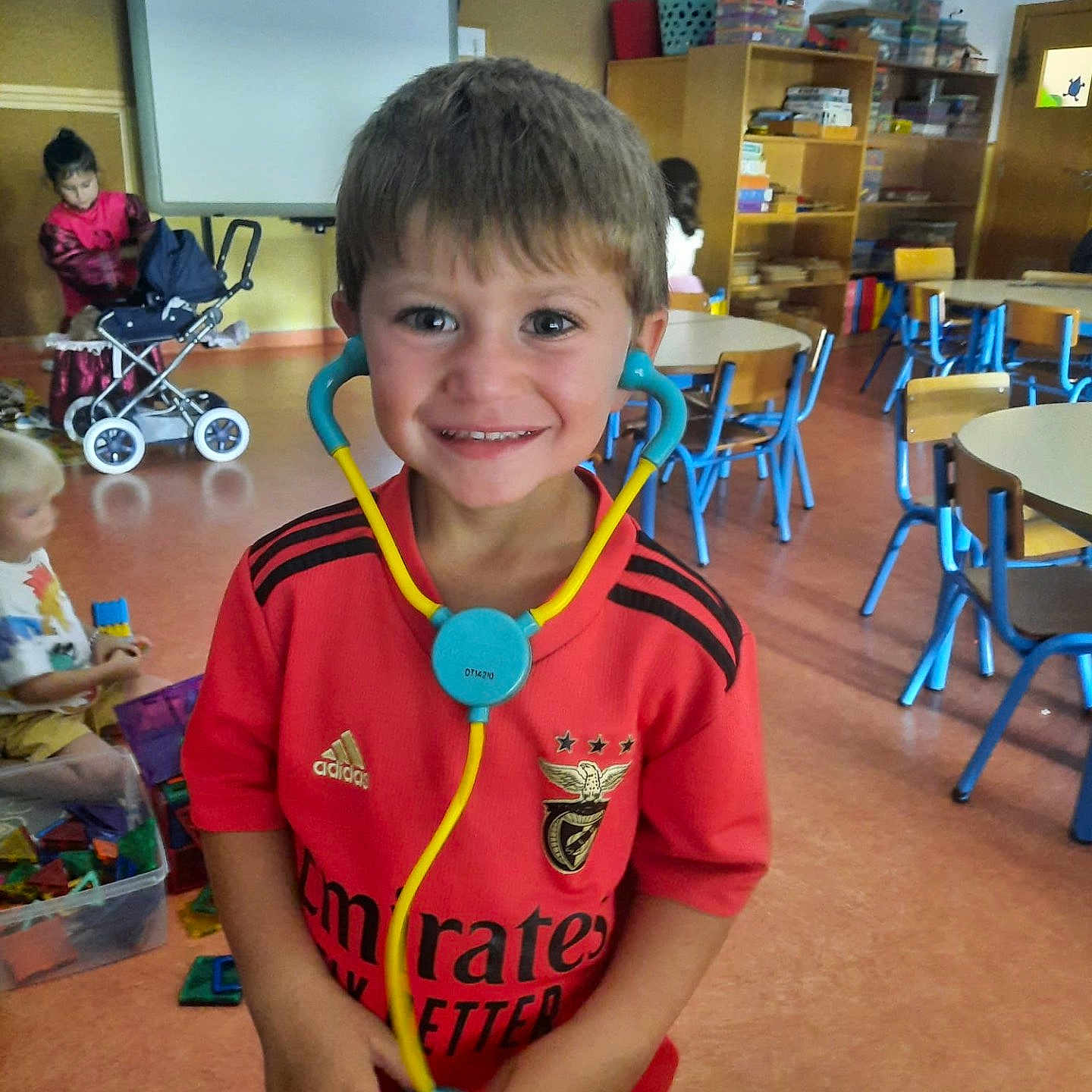 Dani participe au concours pour gagner de l'argent avec cette photo : boy, casual_clothing, chairs, child, classroom, education, furniture, happy, indoor, kids, learning, person, play, red_shirt, school, smiling, stethoscope, tables, toy, toys
