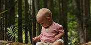 Mavis is registered to the contest to win money with this photo: baby, barefoot, casual_clothing, child, curious, daylight, exploring, forest, greenery, leaves, log, moss, nature, outdoor, pink_shirt, sitting, tree, trunk, woodland, young_child