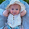 Billie is registered to the contest to win money with this photo: baby, child, infant, hat, sunhat, dress, floral, tongue_out, cute, smiling, outdoor, greenery, seat, cushion, playful, comfort, summer, sunshine, baby_accessory, relaxed