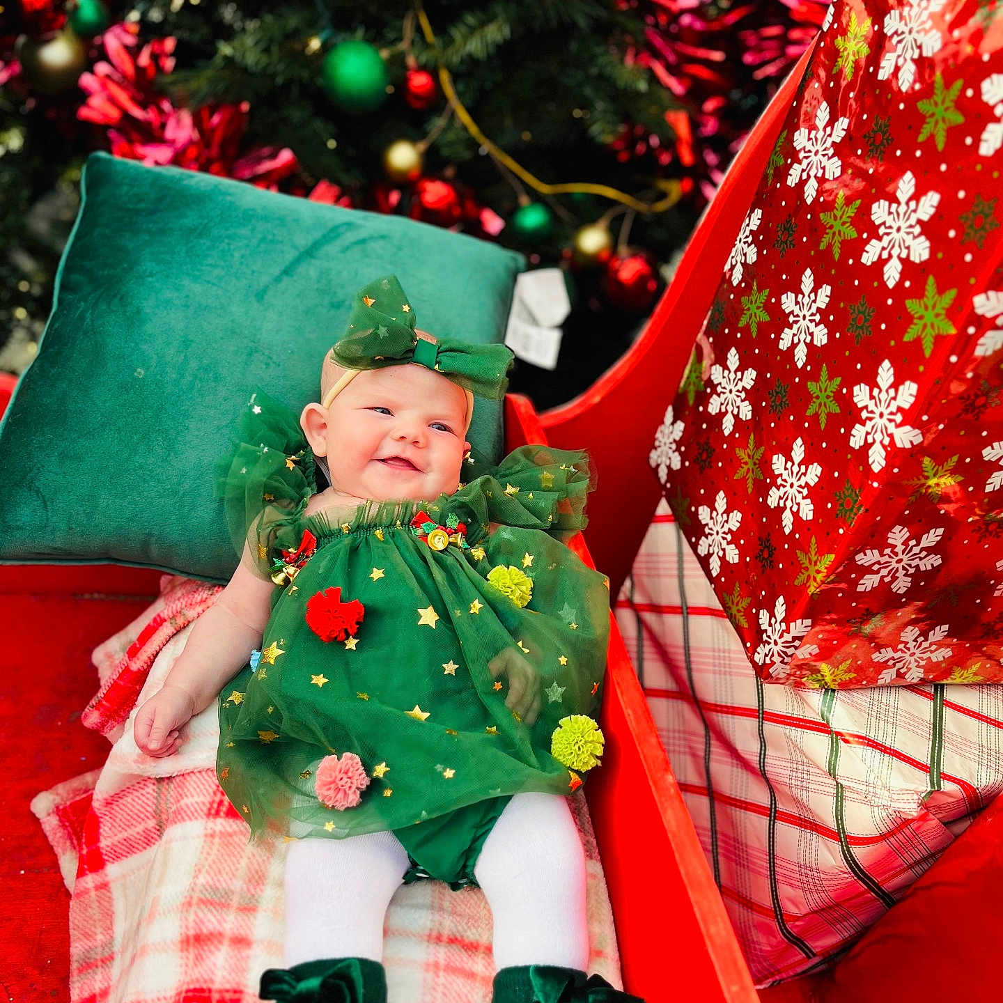 Rosealyn is registered to the contest to win money with this photo: baby, celebration, child, christmas_ornaments, christmas_tree, festive, gift, green_boots, green_dress, headband, holiday, holiday_decoration, indoors, plaid_blanket, pompoms, present, red_sleigh, seasonal, smiling, white_tights